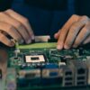 Close-up of hands assembling electronic components on a motherboard in a tech setting.